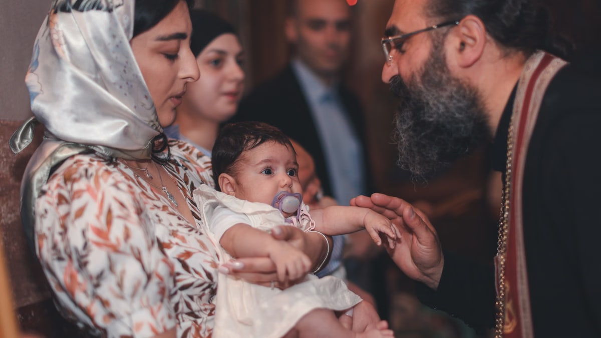 A touching moment during a baby's baptism ceremony, featuring a priest and family.